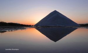 βουνά αλατιού στις αλυκές Μεσολογίου. Το αλάτι μοιάζει με πυραμίδα καθώς καθρεφτίζεται στην λιμνοθάλασσα, που έχει πορτοκαλιά χρώματα, μιας και εκείνη τη στιγμή δύει ο ήλιος